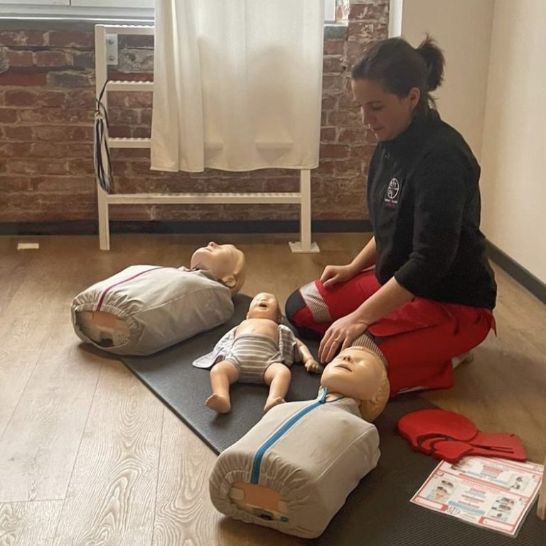Frau übt Erste Hilfe mit Übungspuppen auf einer Matte in einem Trainingsraum.