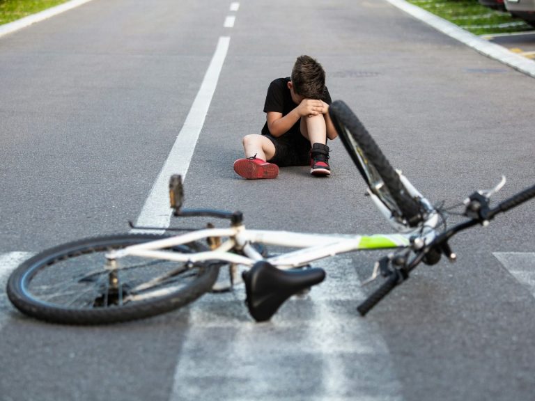 Ein verletzter Junge sitzt auf der Straße neben einem umgekippten Fahrrad.