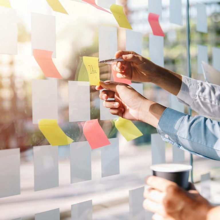 Hände befestigen bunte Notizen an einer Glaswand, Tasse in der anderen Hand.
