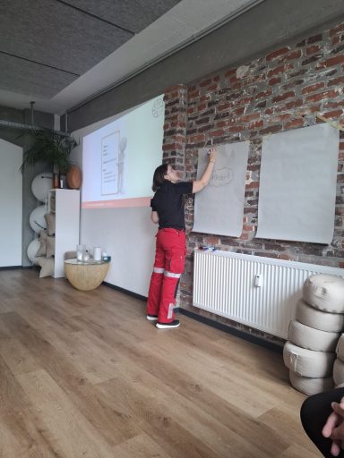 Person in roter Hose schreibt an eine Wandtafel in einem modernen Raum.