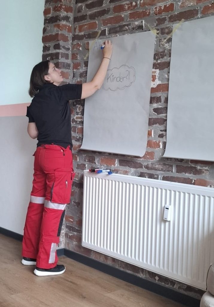 Eine Person mit roten Hosen zeichnet an einer grauen Wandtafel.