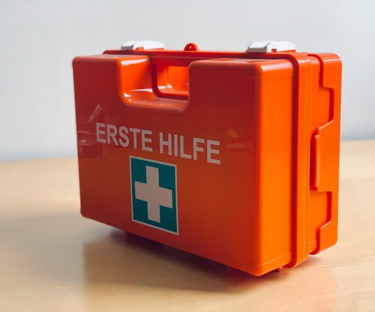 Rettungsbox in Orange mit dem Begriff „Erste Hilfe“ und grünem Kreuz.