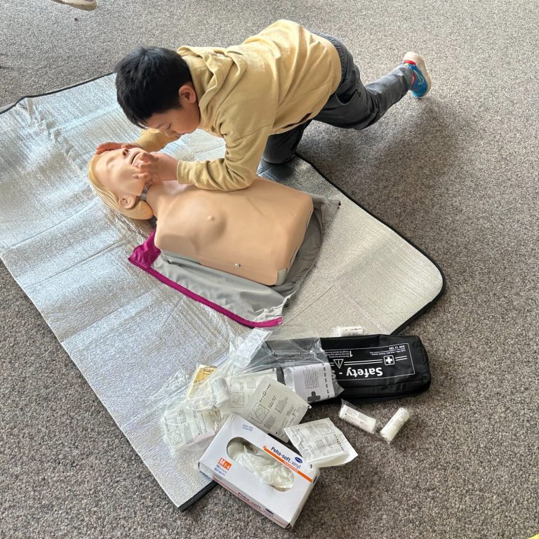 Kind übt Wiederbelebung an einer Übungspuppe auf einem Bodenmatte.