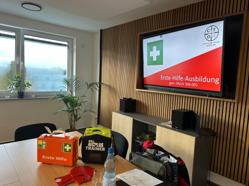 Ein Meetingraum mit einem Bildschirm, Erste-Hilfe-Ausrüstung und Pflanzen im Hintergrund.