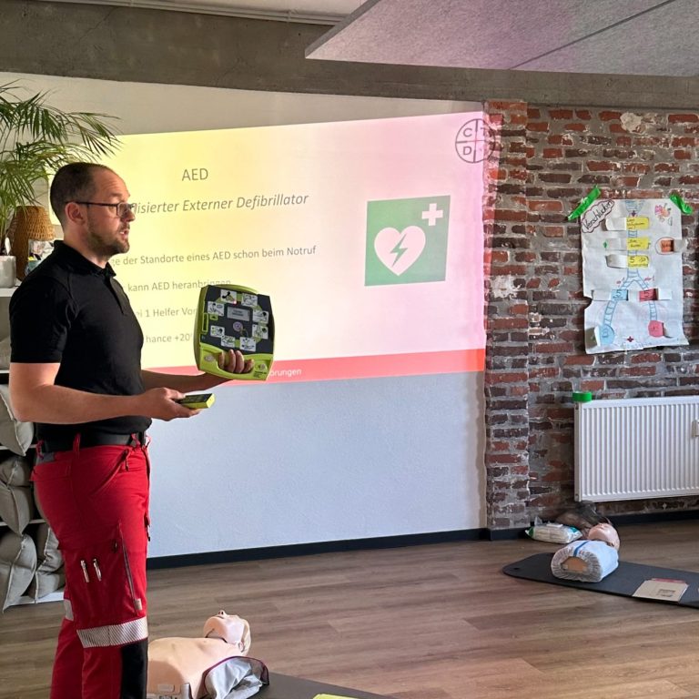 Mann in Uniform hält Defibrillator vor Präsentation über Erste Hilfe.