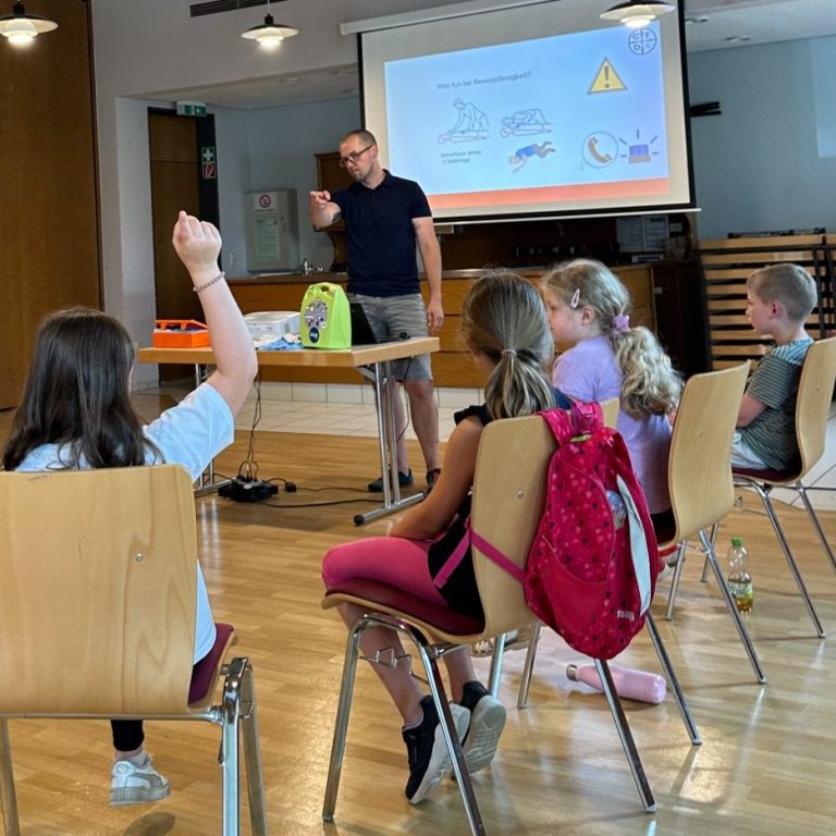 Erste Hilfe Ausbilder präseniert vor einer Gruppe von Kindern in einem Klassenraum.